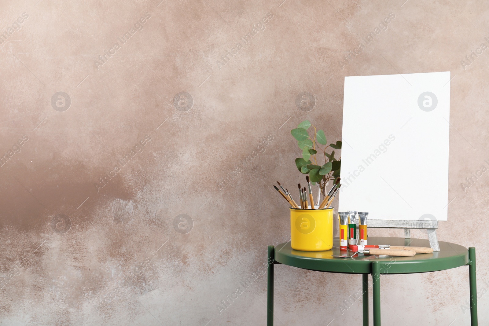 Photo of Wooden easel with blank canvas board and painting tools for children on table near color wall. Space for text