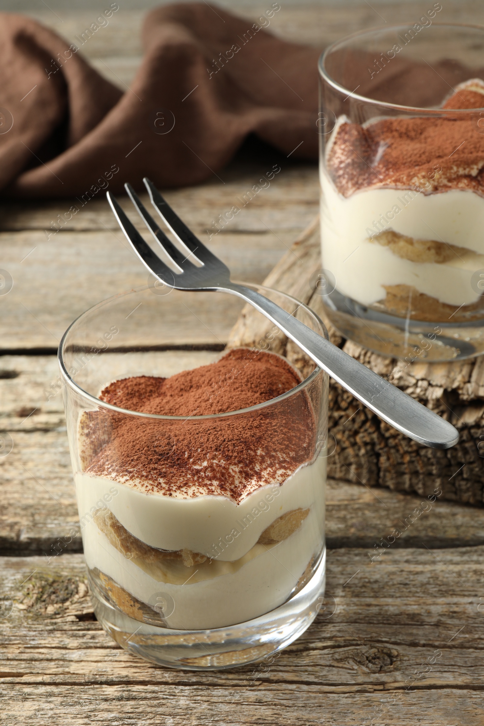 Photo of Delicious tiramisu in glasses and fork on wooden table