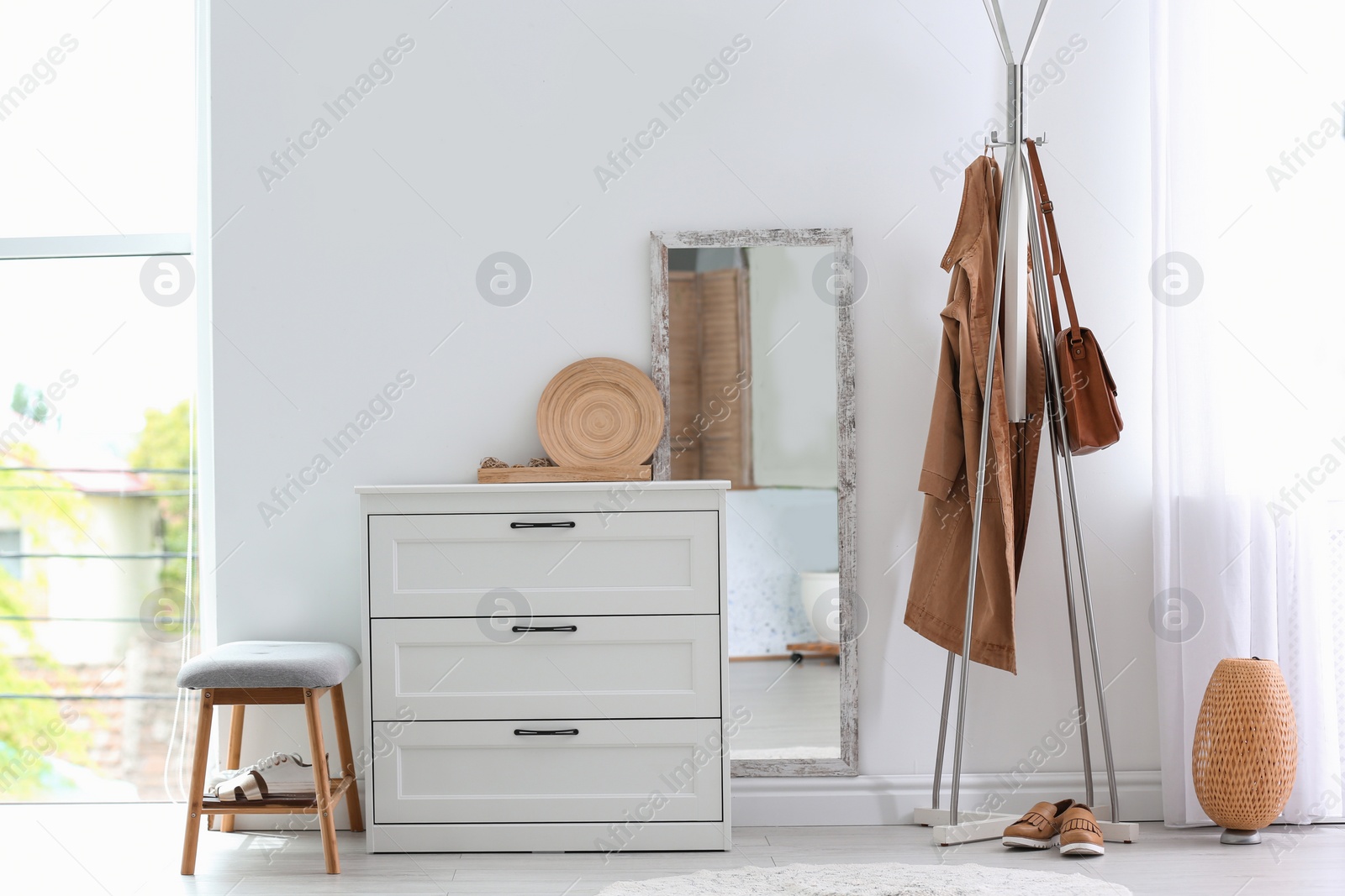 Photo of Modern hallway interior with chest of drawers and clothes on hanger stand. Space for text