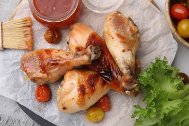 Photo of Marinade, basting brush, roasted chicken drumsticks, tomatoes and lettuce on table, flat lay