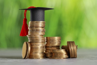 Photo of Scholarship concept. Coins and graduation cap on grey table against blurred background, closeup