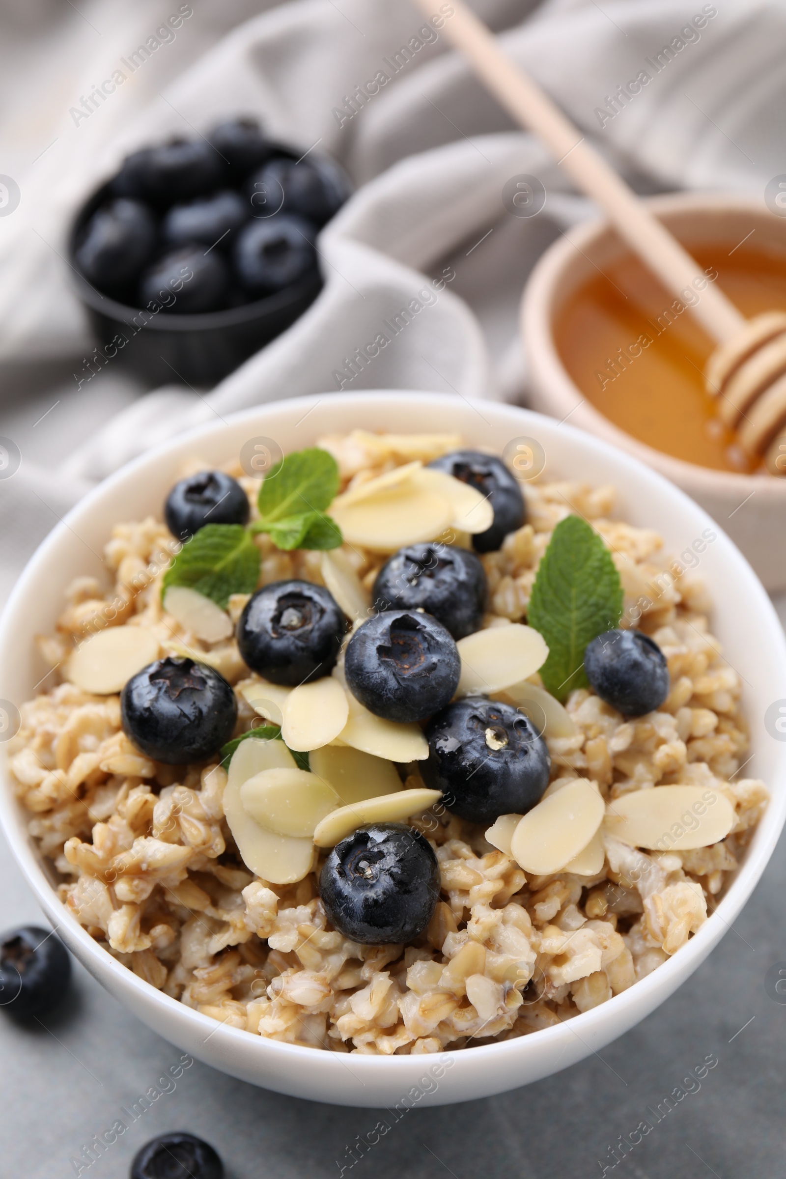 Photo of Tasty oatmeal with blueberries, mint and almond petals in bowl on grey table, closeup