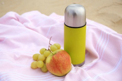 Metallic thermos with hot drink, fruits and plaid on sandy beach, closeup