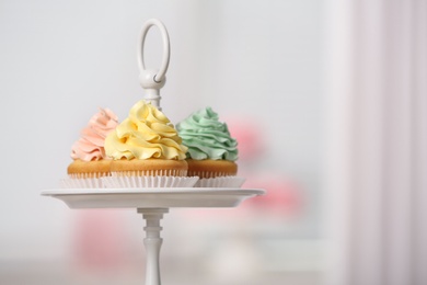 Photo of Stand with colorful cupcakes against blurred background, space for text. Candy bar