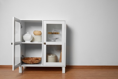 Photo of Wooden cabinet with kitchenware near white wall, space for text