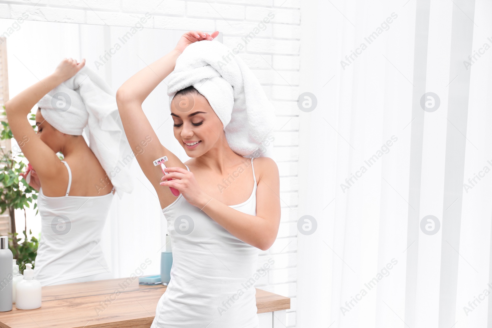 Photo of Beautiful young woman shaving armpit at home. Space for text