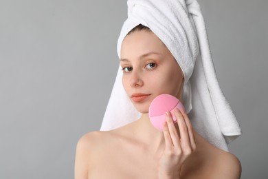 Photo of Washing face. Young woman with cleansing brush on grey background