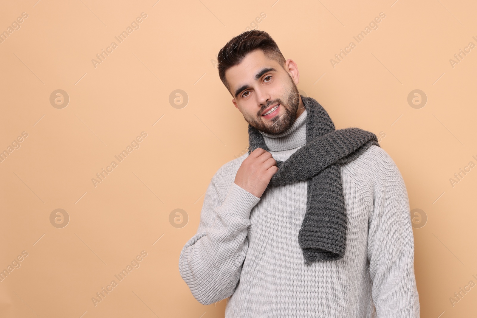 Photo of Smiling man in knitted scarf on beige background. Space for text