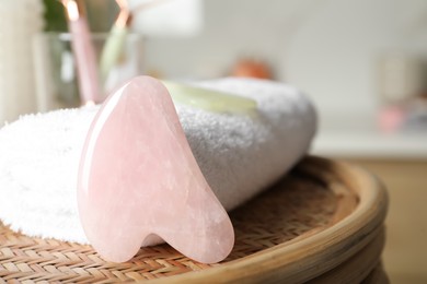 Photo of Rose quartz gua sha tool and soft towel on wicker table indoors, closeup. Space for text