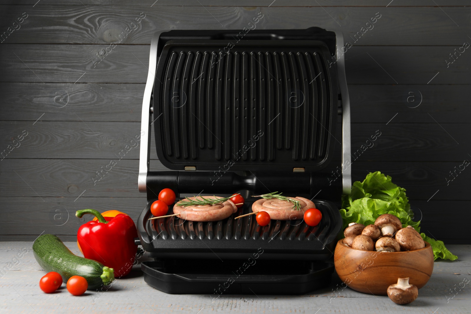 Photo of Electric grill with homemade sausages, rosemary and vegetables on rustic wooden table