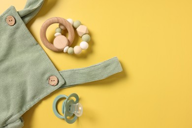 Baby accessories. Rattle, pacifier and overall on yellow background, flat lay. Space for text