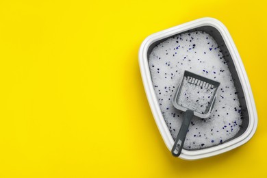 Photo of Cat litter tray with filler and scoop on yellow background, top view. Space for text
