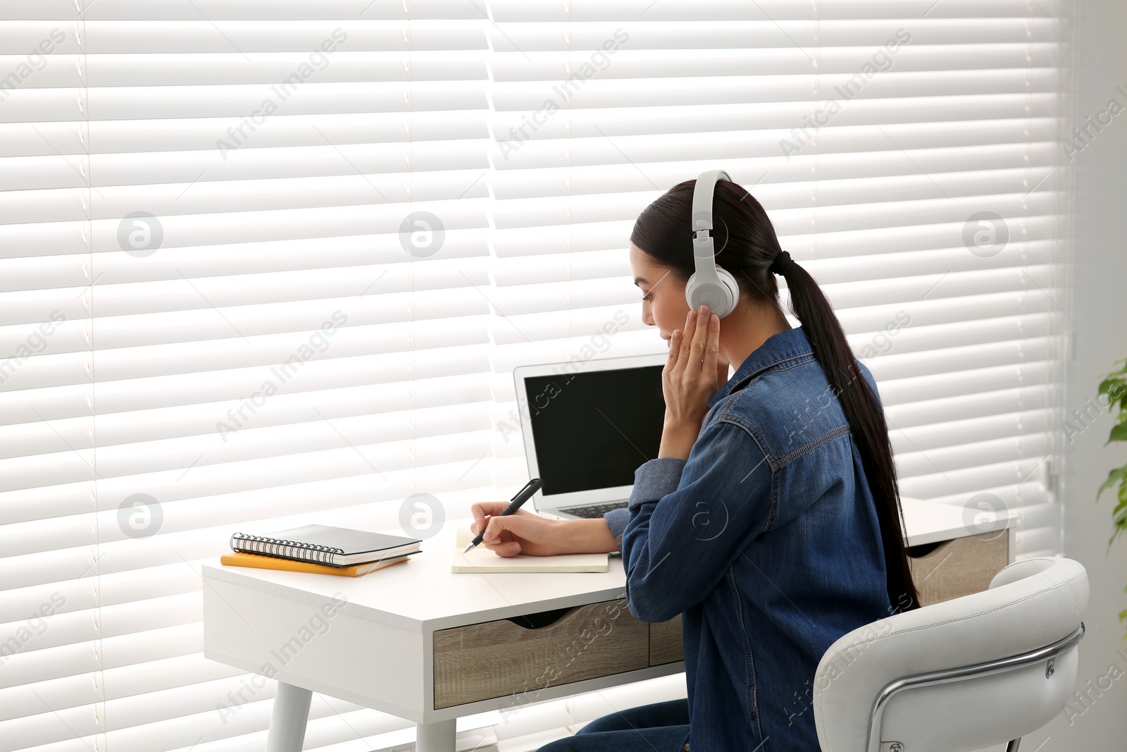 Photo of Online translation course. Student in headphones writing near laptop indoors, space for text