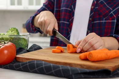 Woman cutting carrot at table in kitchen, closeup. Food storage