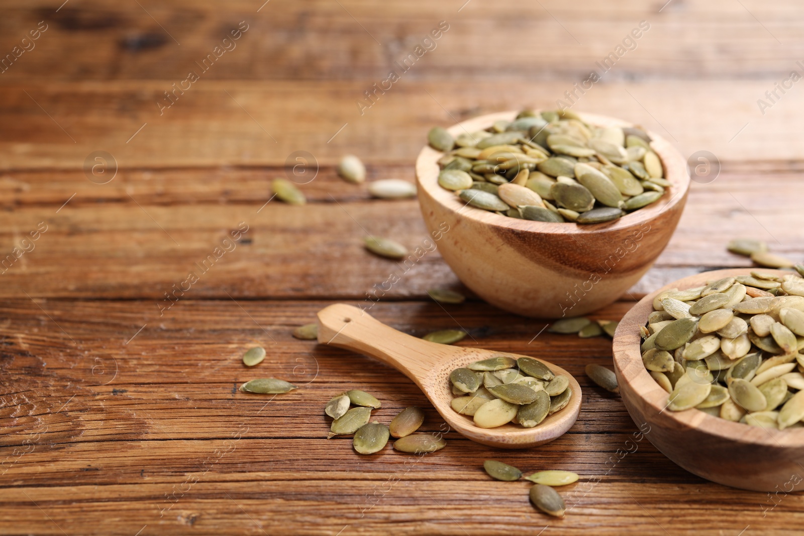 Photo of Bowls and spoon with peeled pumpkin seeds on wooden table. Space for text