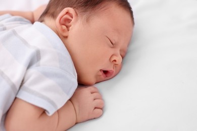 Cute newborn baby sleeping on white bed, closeup. Space for text