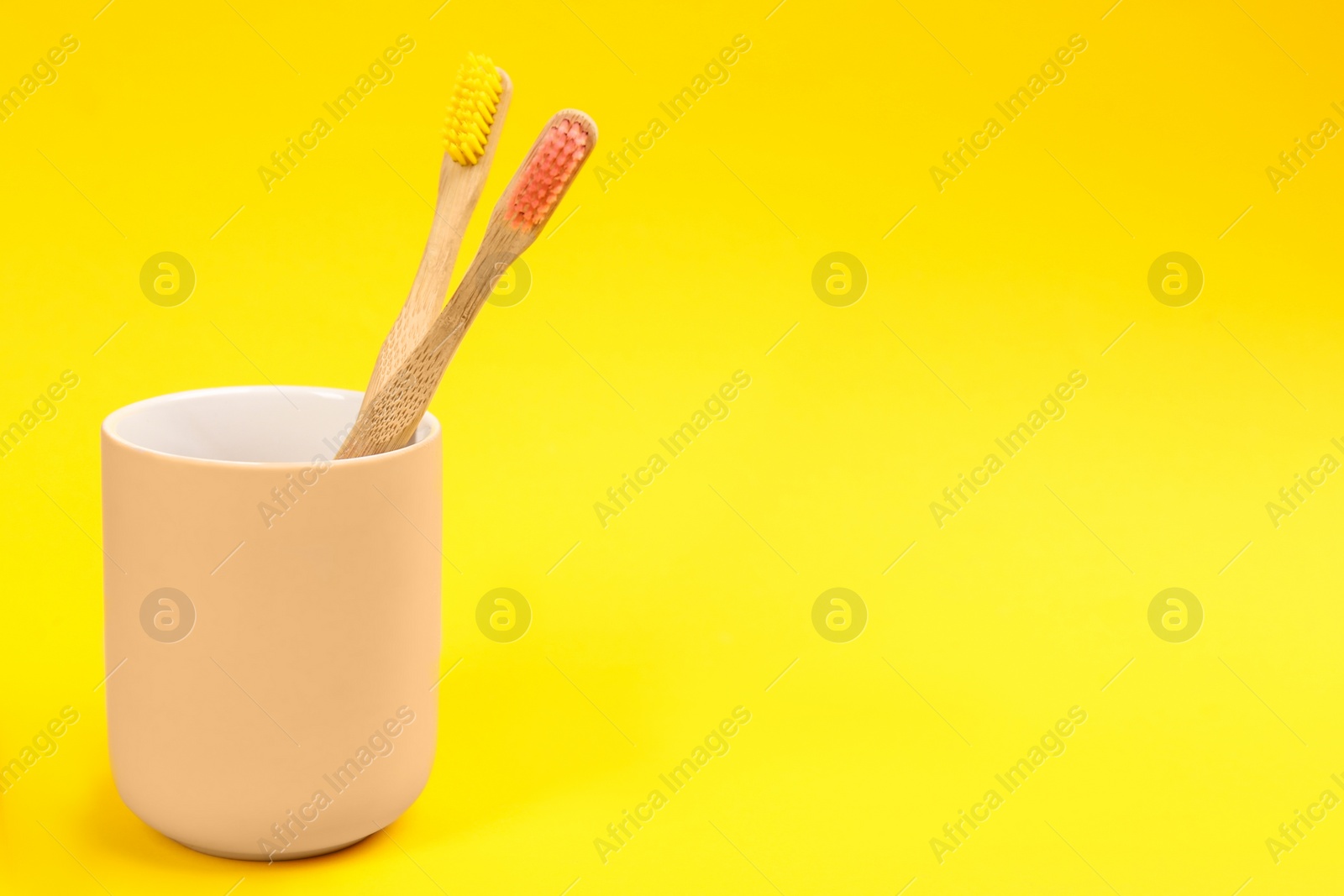 Photo of Toothbrushes made of bamboo in holder on yellow background. Space for text