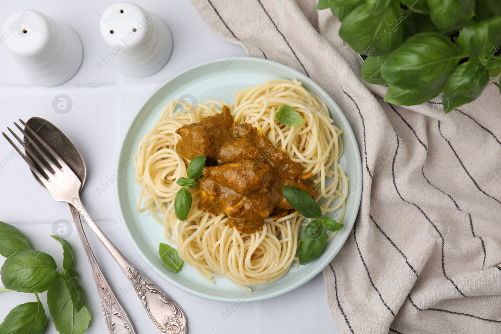 Photo of Delicious pasta and chicken with curry sauce served on white tiled table, flat lay