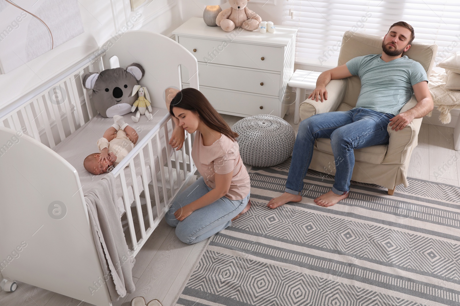 Photo of Tired young parents and their baby sleeping in children's room