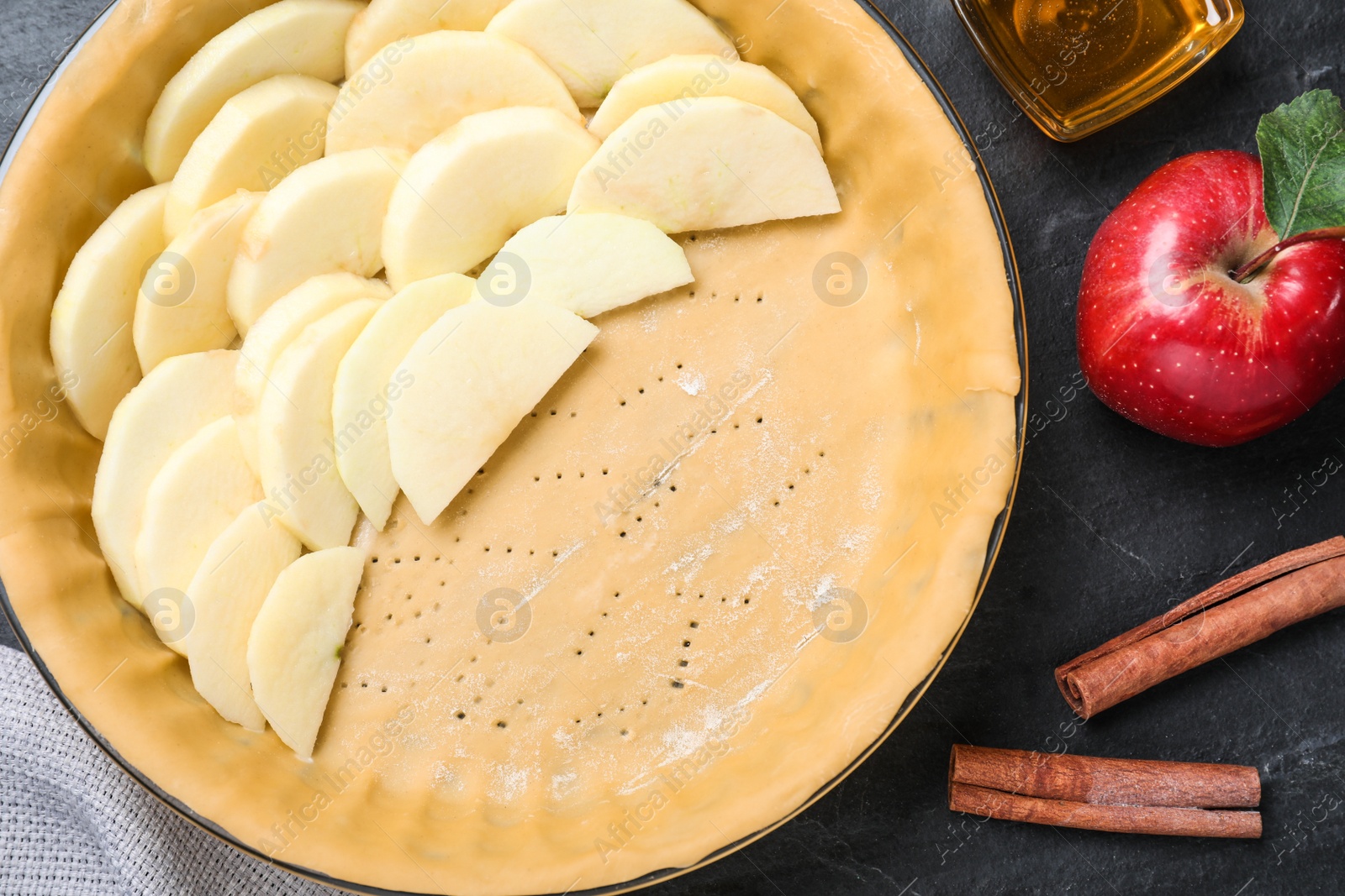 Photo of Dish with fresh apple slices and raw dough on black table, flat lay. Baking pie