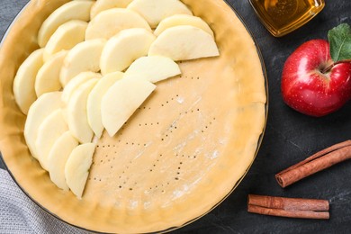 Dish with fresh apple slices and raw dough on black table, flat lay. Baking pie