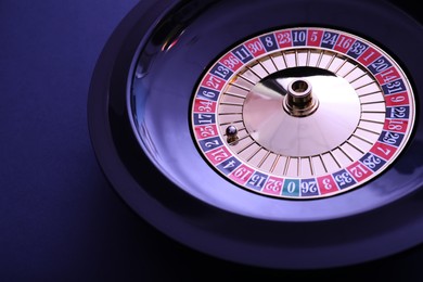 Photo of Roulette wheel with ball on dark violet background, closeup. Casino game