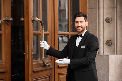 Photo of Butler in elegant suit and white gloves opening wooden hotel door