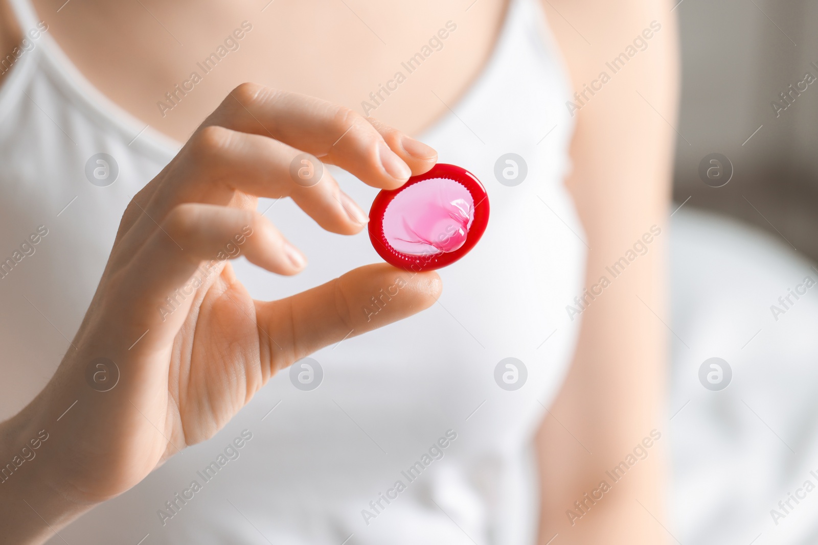 Photo of Woman holding unpacked condom on blurred background, closeup. Safe sex