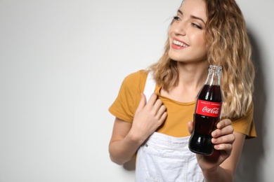 Photo of MYKOLAIV, UKRAINE - NOVEMBER 28, 2018: Young woman with bottle of Coca-Cola on white background, space for text