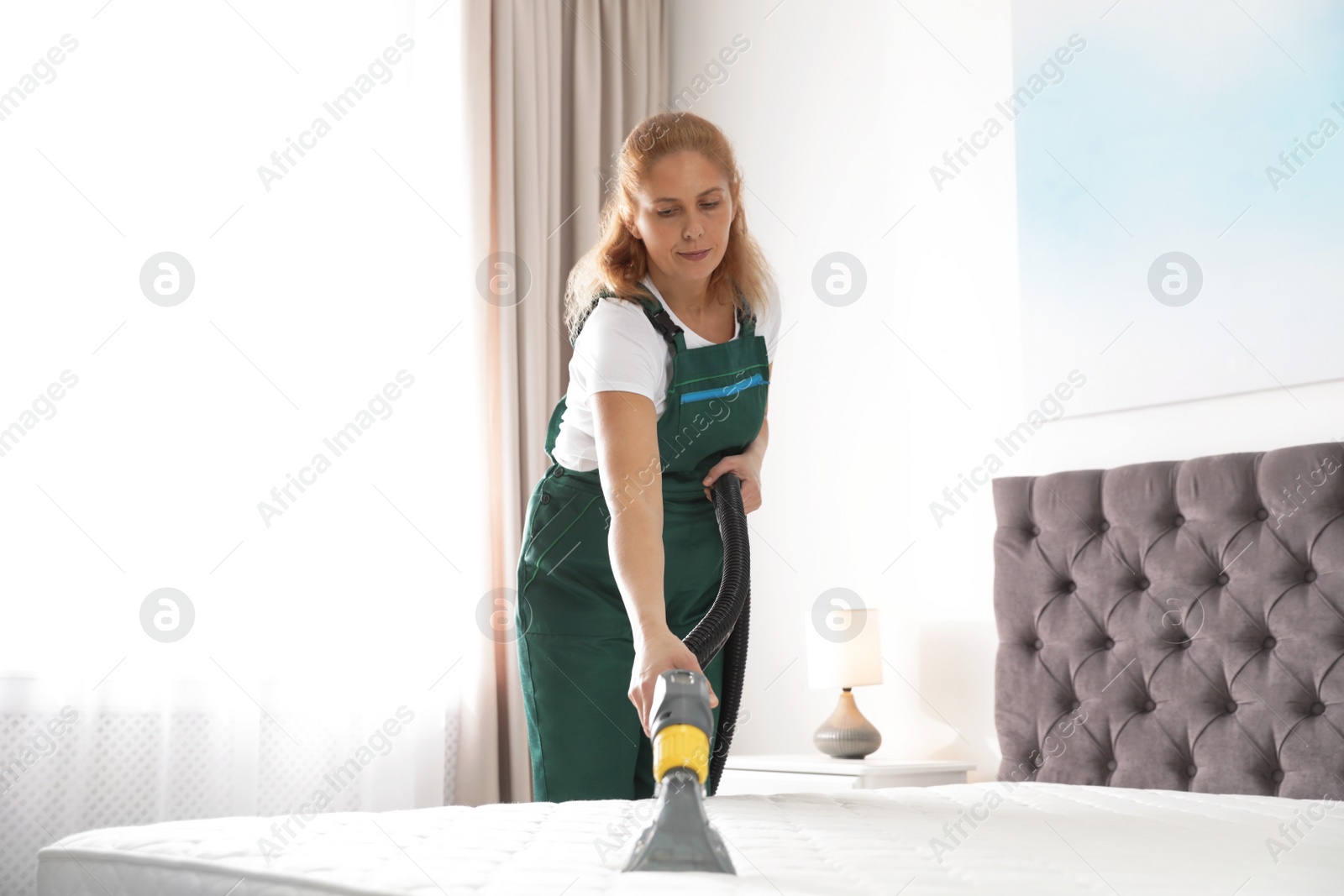 Photo of Janitor cleaning mattress with professional equipment in bedroom