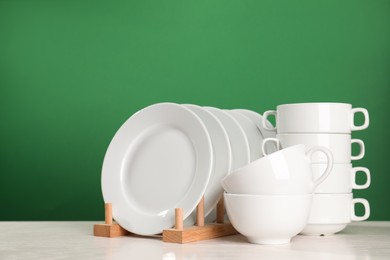 Set of clean dishware on white table against green background