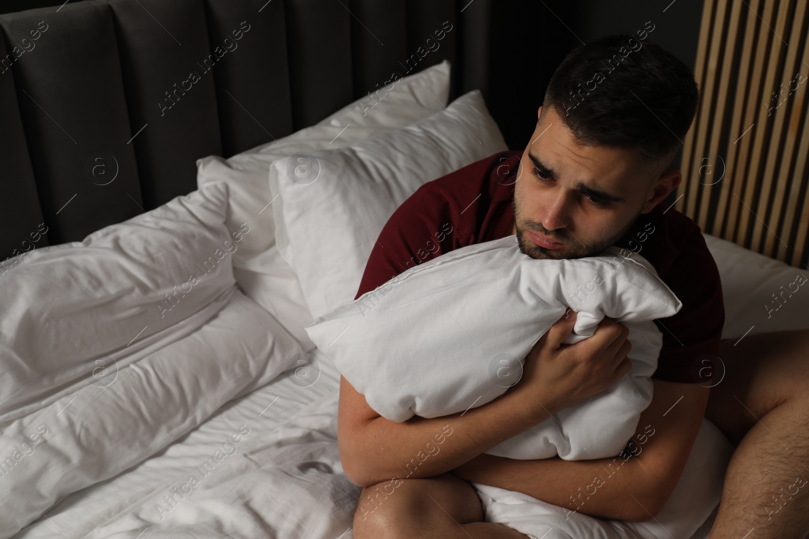 Photo of Sad man hugging pillow on bed at home. Space for text