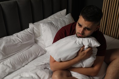 Photo of Sad man hugging pillow on bed at home. Space for text