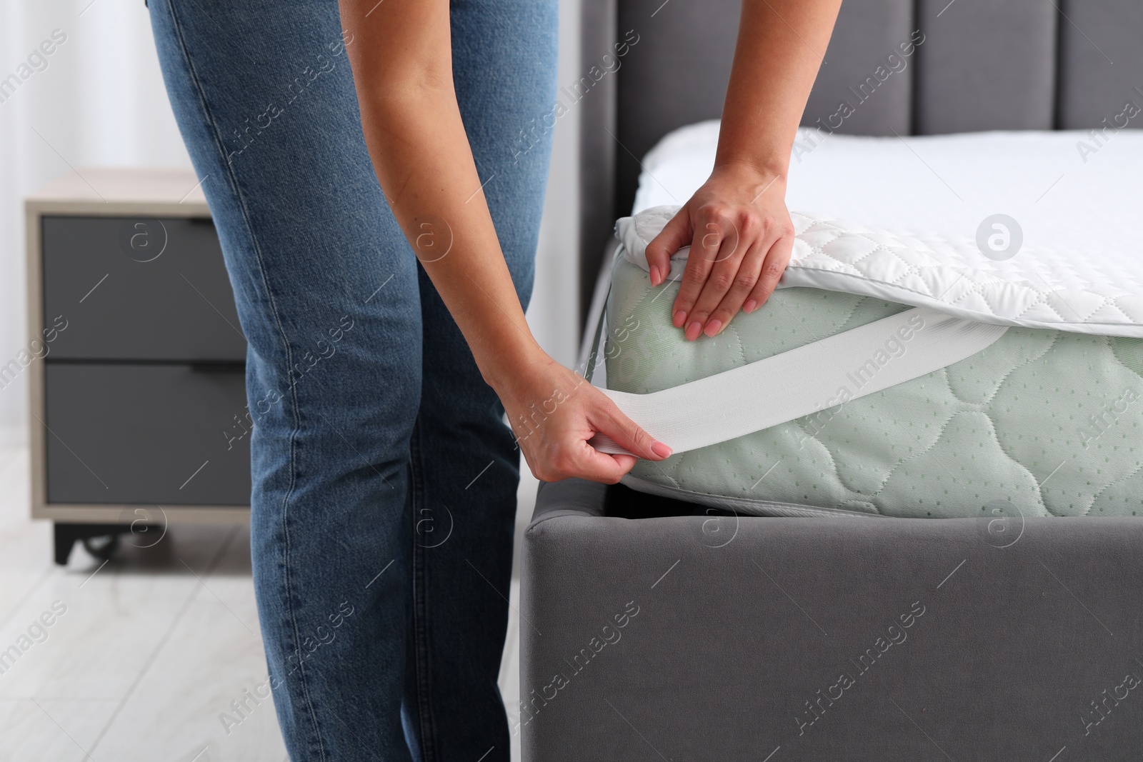 Photo of Woman putting protector on mattress in bedroom, closeup