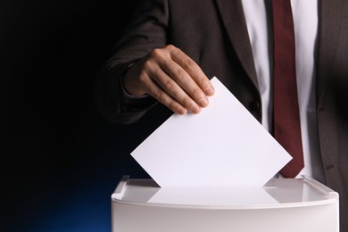 Photo of Man putting his vote into ballot box on dark blue background, closeup. Space for text