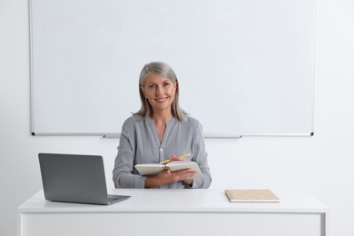 Photo of Happy professor giving lecture near laptop at desk in classroom, space for text