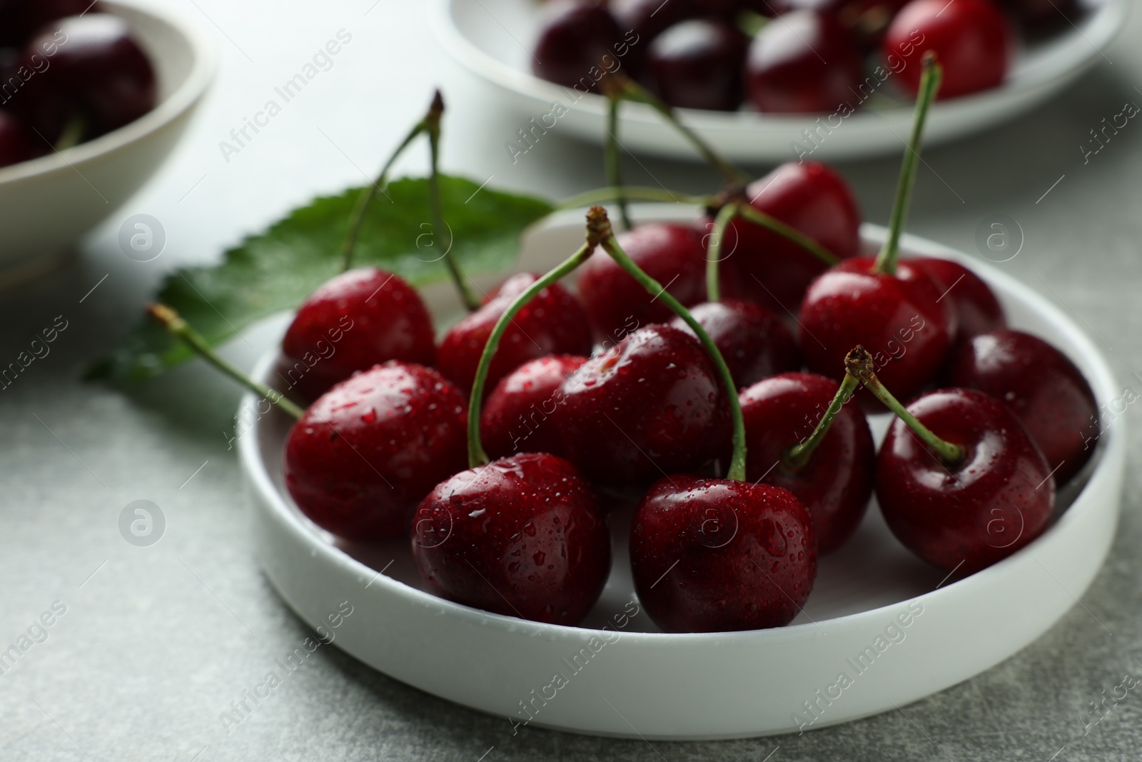 Photo of Fresh ripe cherries with water drops on light grey table, closeup