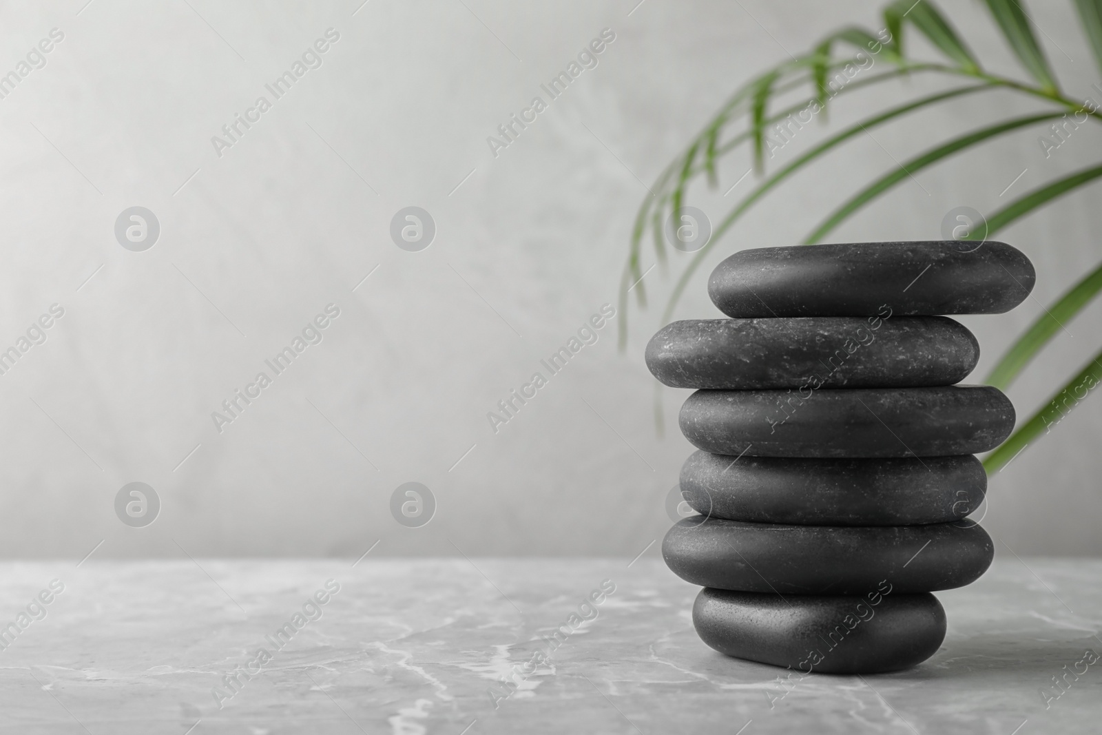 Photo of Stack of spa stones and palm leaf on grey table, space for text