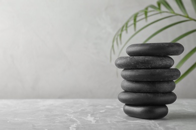 Photo of Stack of spa stones and palm leaf on grey table, space for text