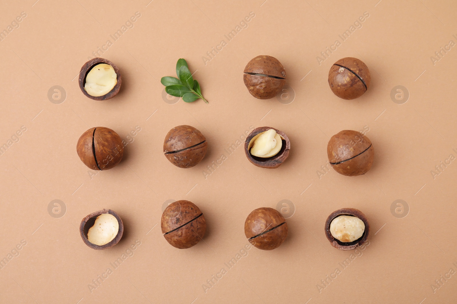 Photo of Tasty Macadamia nuts and green leaves on beige background, flat lay