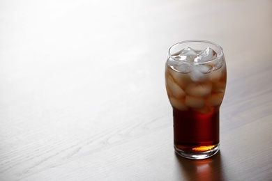 Photo of Glass of cola with ice on wooden background, space for text