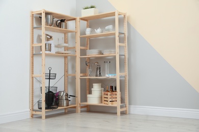 Wooden shelving units with kitchenware near color wall, space for text. Stylish room interior