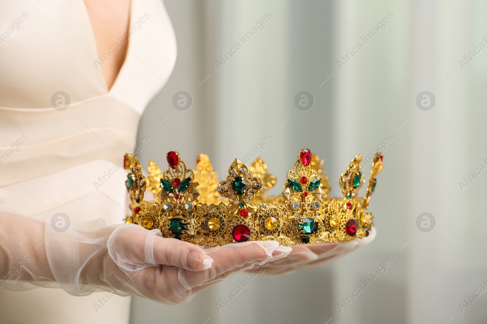 Photo of Bride holding luxurious crown on blurred background, closeup view