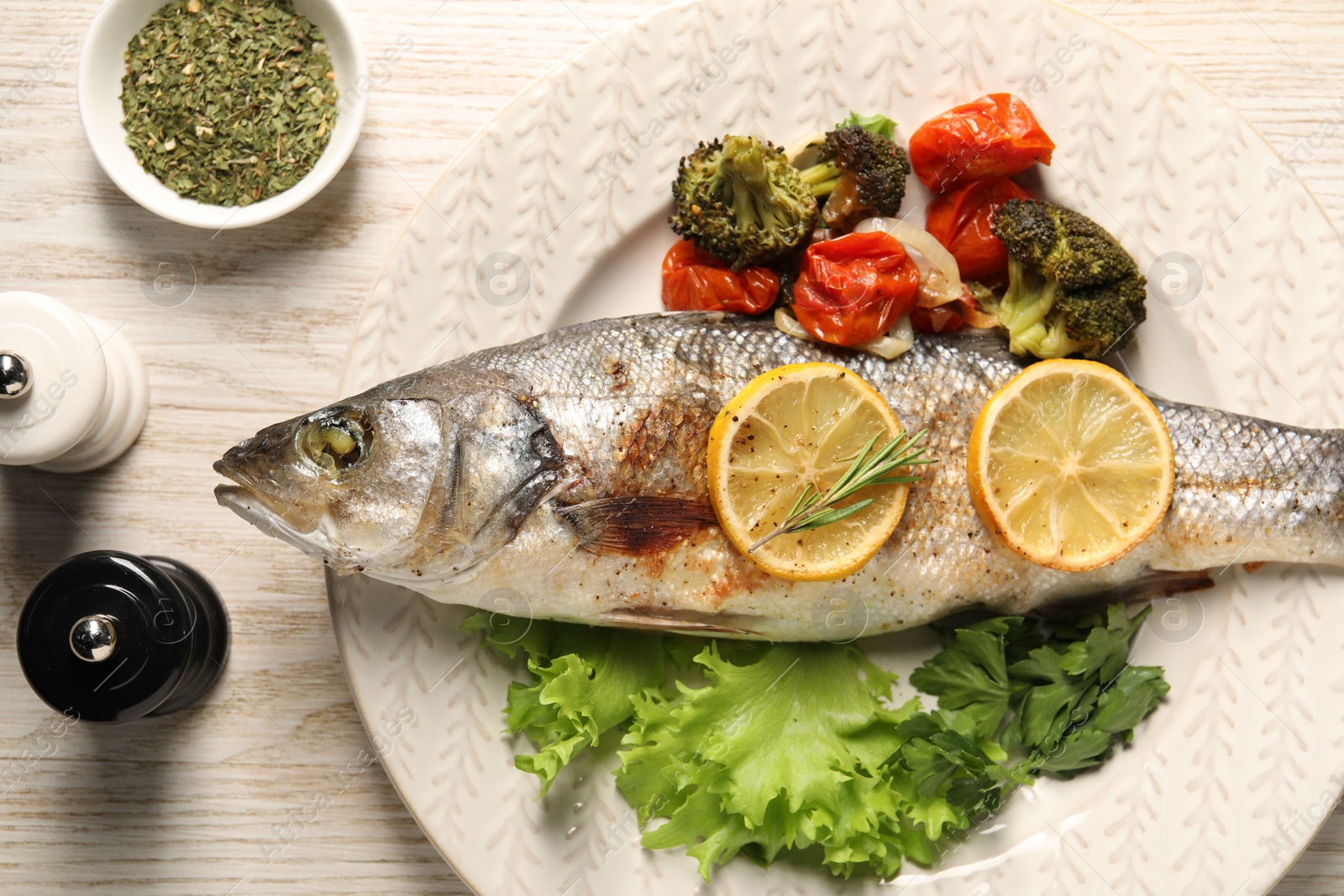 Photo of Delicious baked fish and vegetables served on wooden table, flat lay