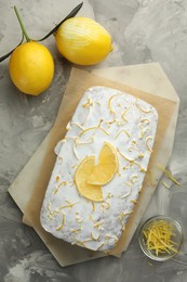 Photo of Tasty lemon cake with glaze, citrus fruits and zest on gray textured table, flat lay