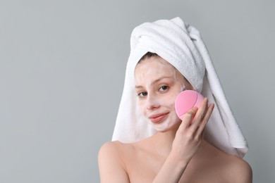 Photo of Young woman washing face with brush and cleansing foam on grey background. Space for text