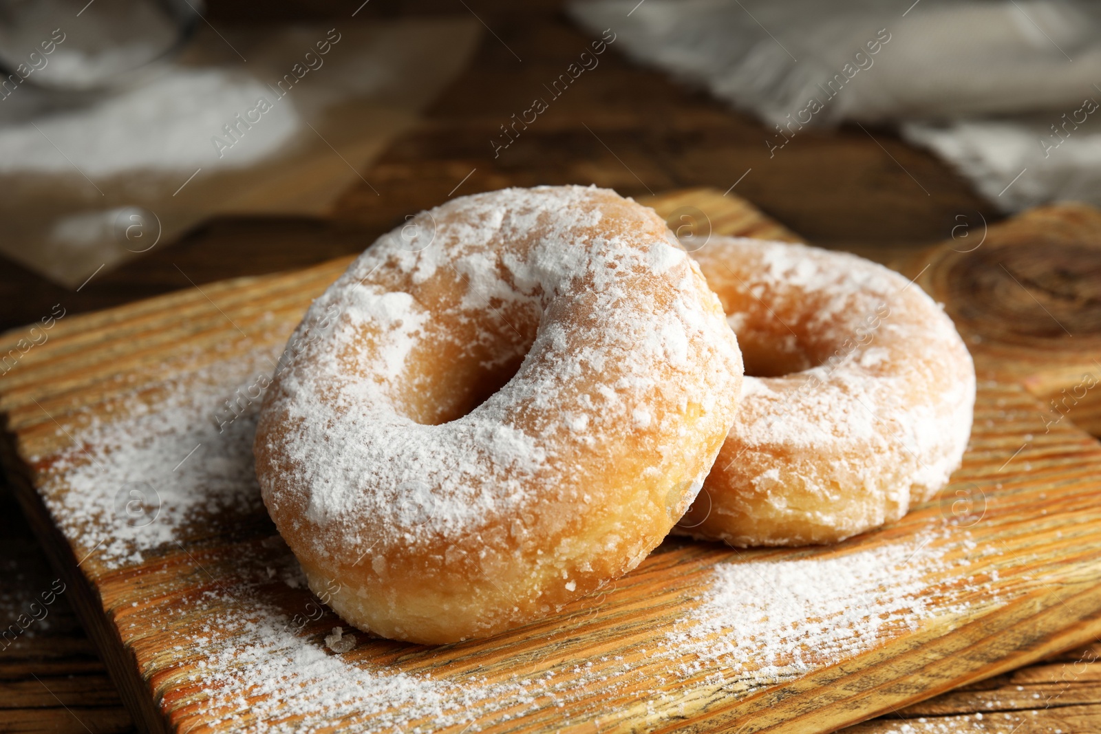 Photo of Delicious donuts with powdered sugar on wooden table