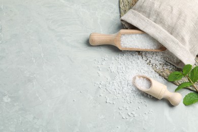 Photo of Wooden scoops with natural sea salt and sack on light grey marble table. Space for text