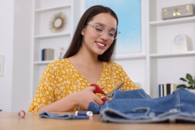 Happy woman cutting hem of jeans at table indoors