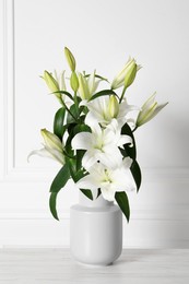 Photo of Beautiful bouquet of lily flowers in vase on light table near white wall